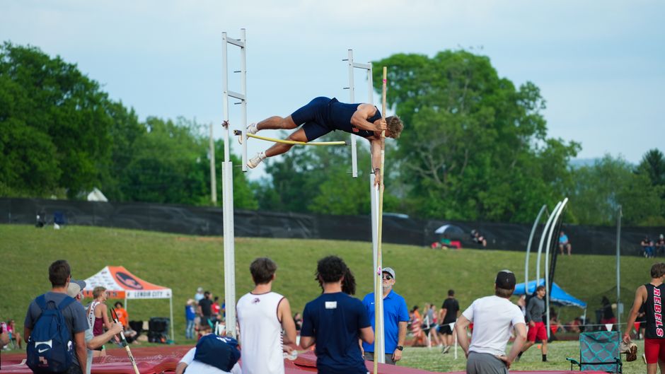 An athlete in action during a pole vault competition at an outdoor sports event with a crowd watching.