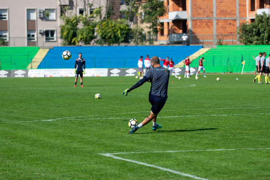 Soccer player kicking a ball during training on a green field under sunny skies.
