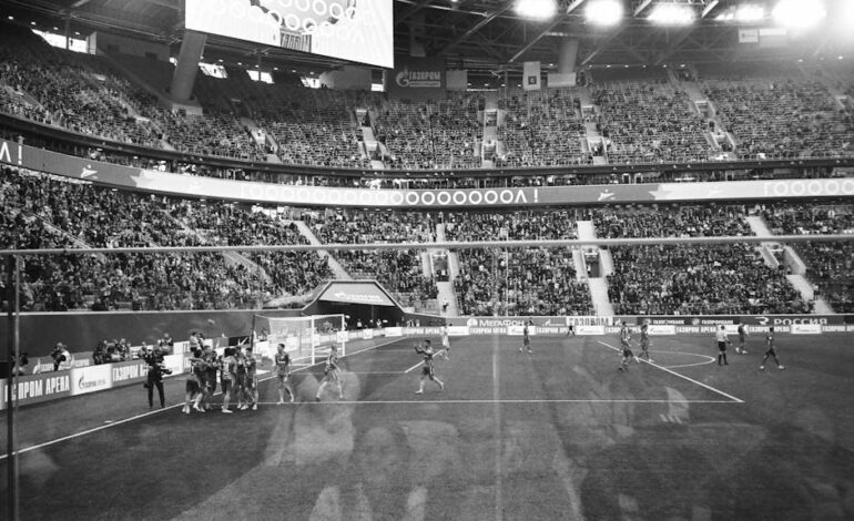 Through glass black and white football team standing together and congratulating each other with match win game in crowded stadium