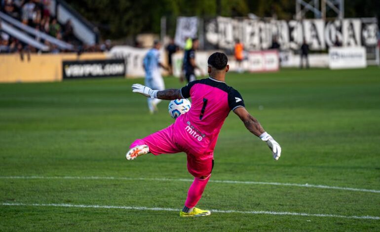 A goalkeeper in bright pink kit kicking a soccer ball during a match.