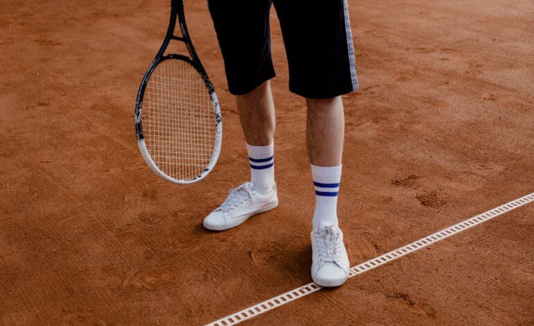 Man standing on a clay tennis court holding a racket, wearing sneakers.