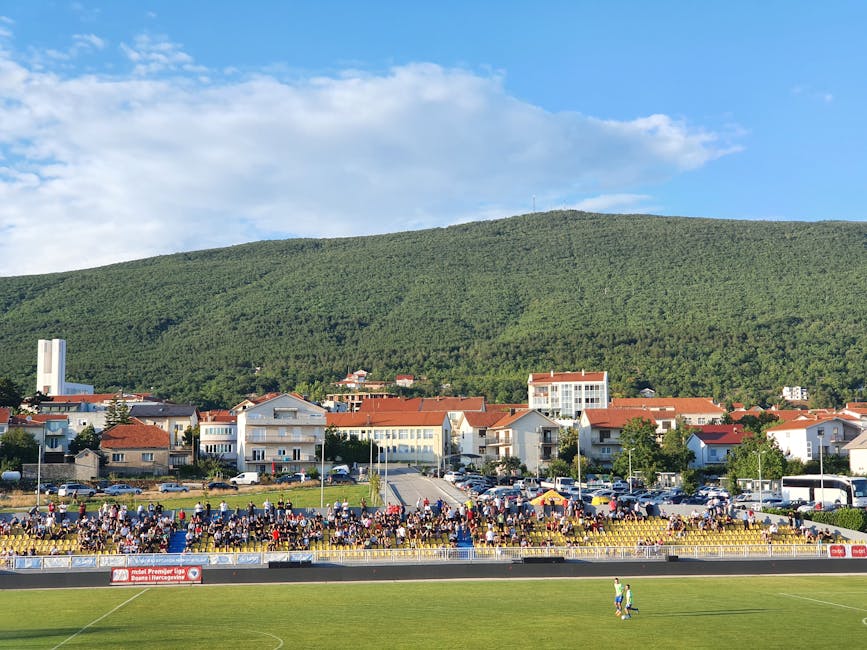 Crowded football stadium in Posušje with lush hills and townscape in the background.