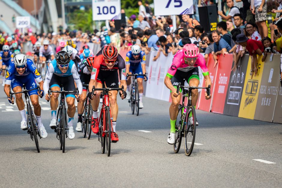 Cyclists compete in an exhilarating road race in bustling Hong Kong city streets, drawing a large crowd.