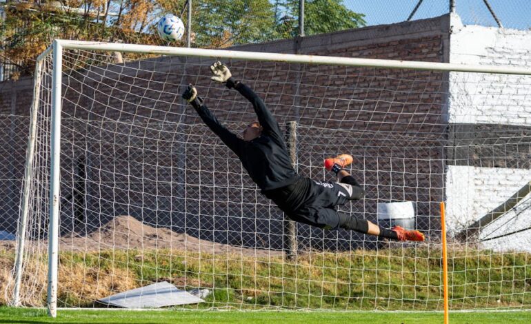 Dynamic action shot of a goalkeeper making a high save during a soccer game outdoors.